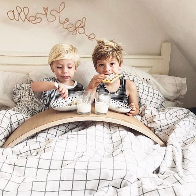 deux enfants assis cote a cote sur un lit, ils prennent leur petit-déjeuner posé sur la wobbel board