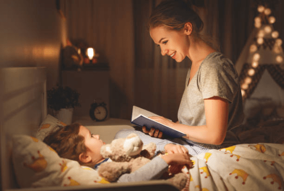 enfant allongé dans son lit, sa maman est assise à coté de lui, elle tient un livre et lui lit une histoire