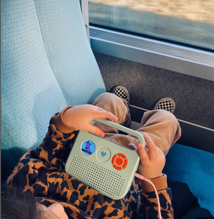 enfant allongé sur le siège d'un train, il tient l'enceinte audio Merlin dans ses mains
